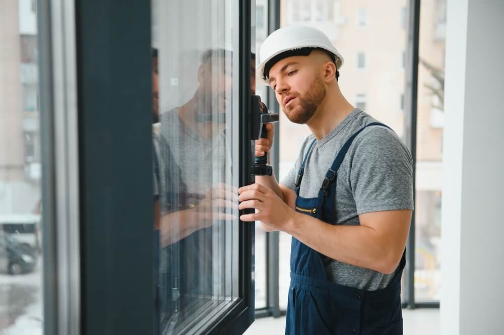 Workman in overalls installing or adjusting plastic windows in the living room at home.