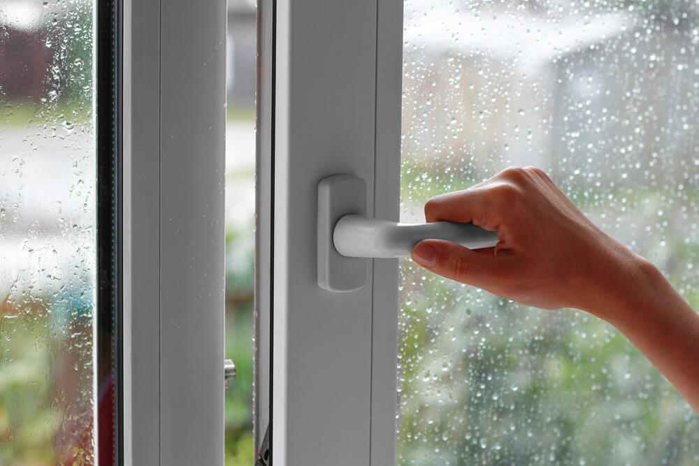 A female hand opens a window with water drops.