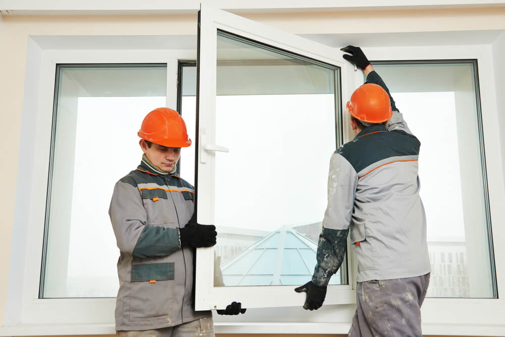 Two male industrial builders work at window installation.
