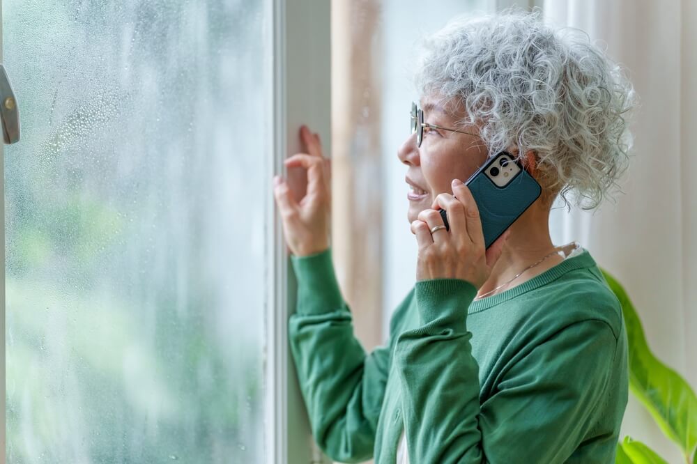 A senior woman is checking out the window while it's storming outside.